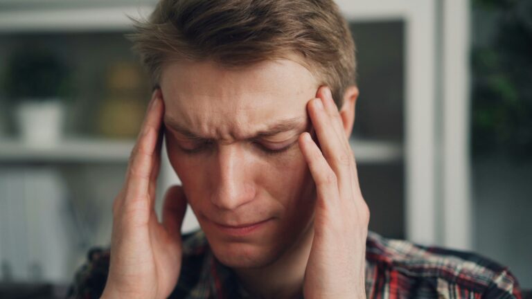 Man with eyes closed, pressing his temples with both hands in apparent headache or stress.
